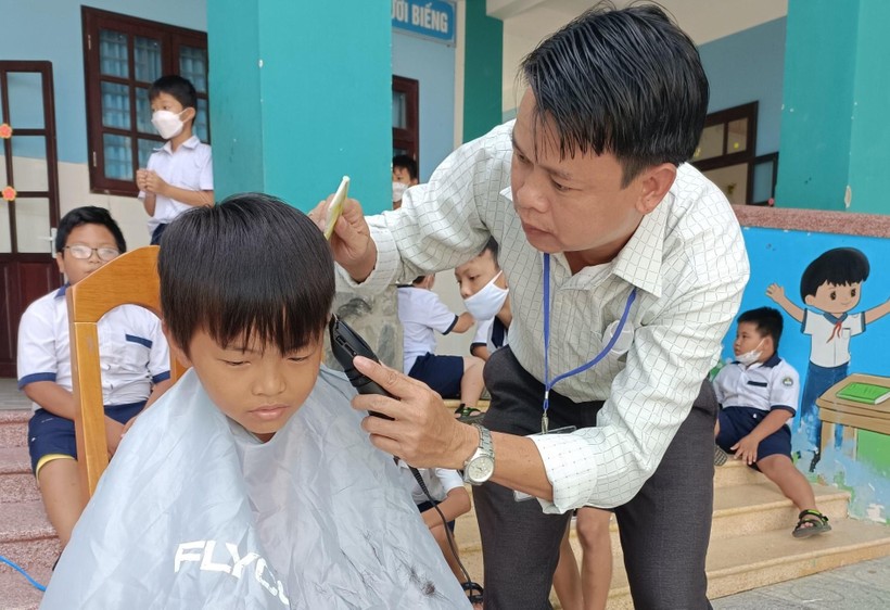 Thầy Bình cắt tóc cho học sinh ngay tại sân trường.